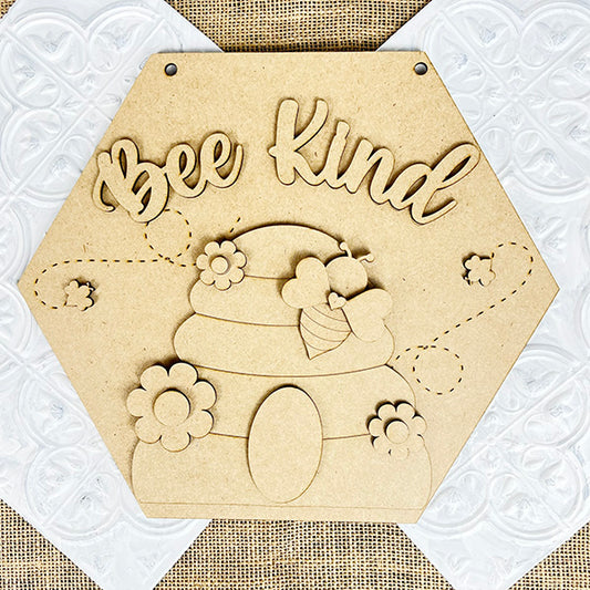 Janet's Craft Corner offers the Bee Kind Door Hanger, a rustic farmhouse hexagonal wooden plaque DIY kit. It features an engraved beehive design with bees and flowers, and "Bee Kind" inscribed above in a charming white decorative pattern. Perfect for seasonal home décor.