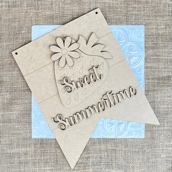 Janet's Craft Corner offers a DIY kit for rustic charm: the Strawberry Door Hanger. It features "Sweet Summertime" in cursive over burlap, set against light blue textured tiles. Perfect for adding sweetness to any space!.