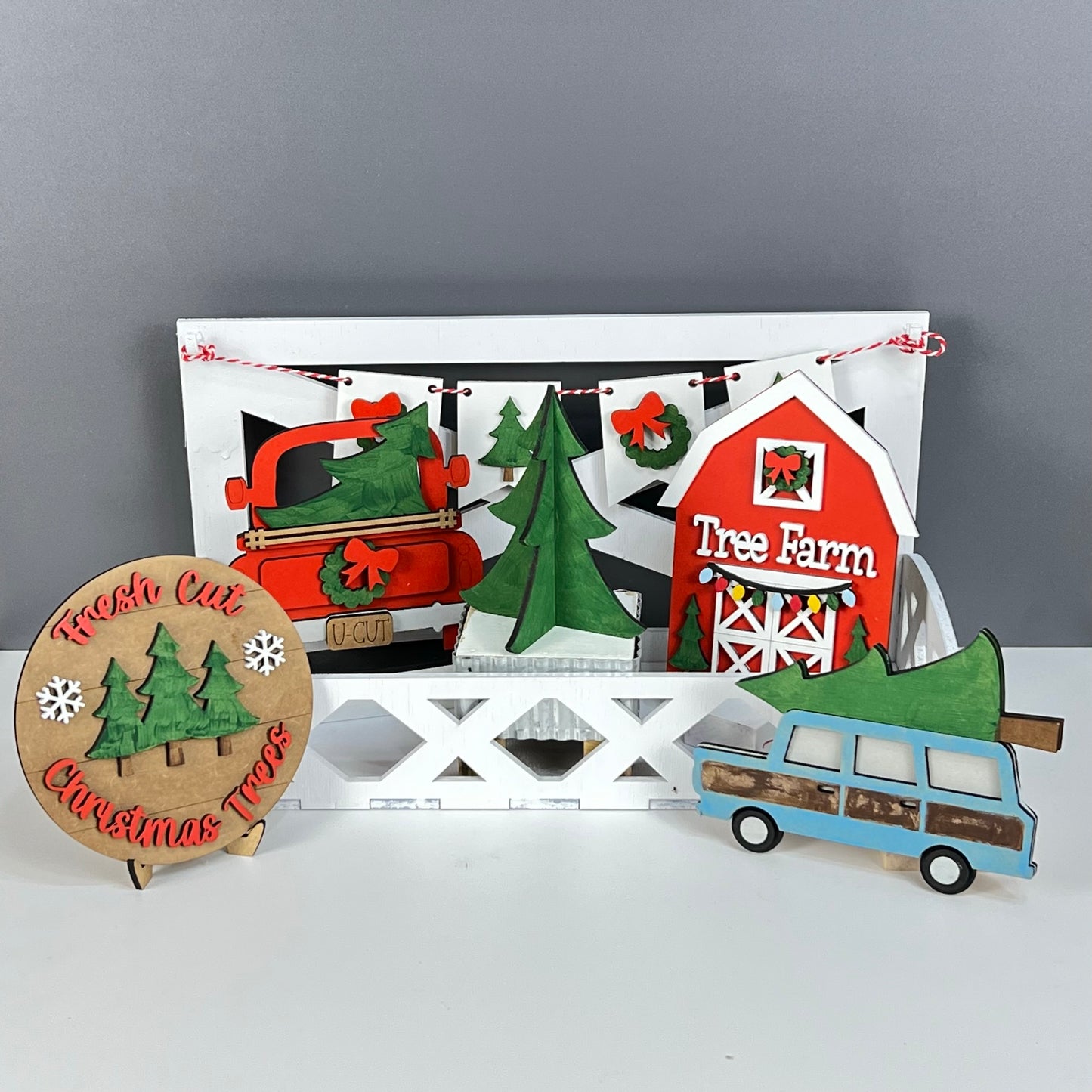 Janet's Craft Corner presents the "Tree Farm - DIY Tiered Tray Kit," featuring charming festive wooden decorations such as a red barn labeled "Tree Farm," a vintage truck, and a nostalgic station wagon carrying a Christmas tree. This delightful kit includes a "Fresh Cut Christmas Trees" sign alongside a green tree, all set against an elegant gray background—ideal for DIY enthusiasts!