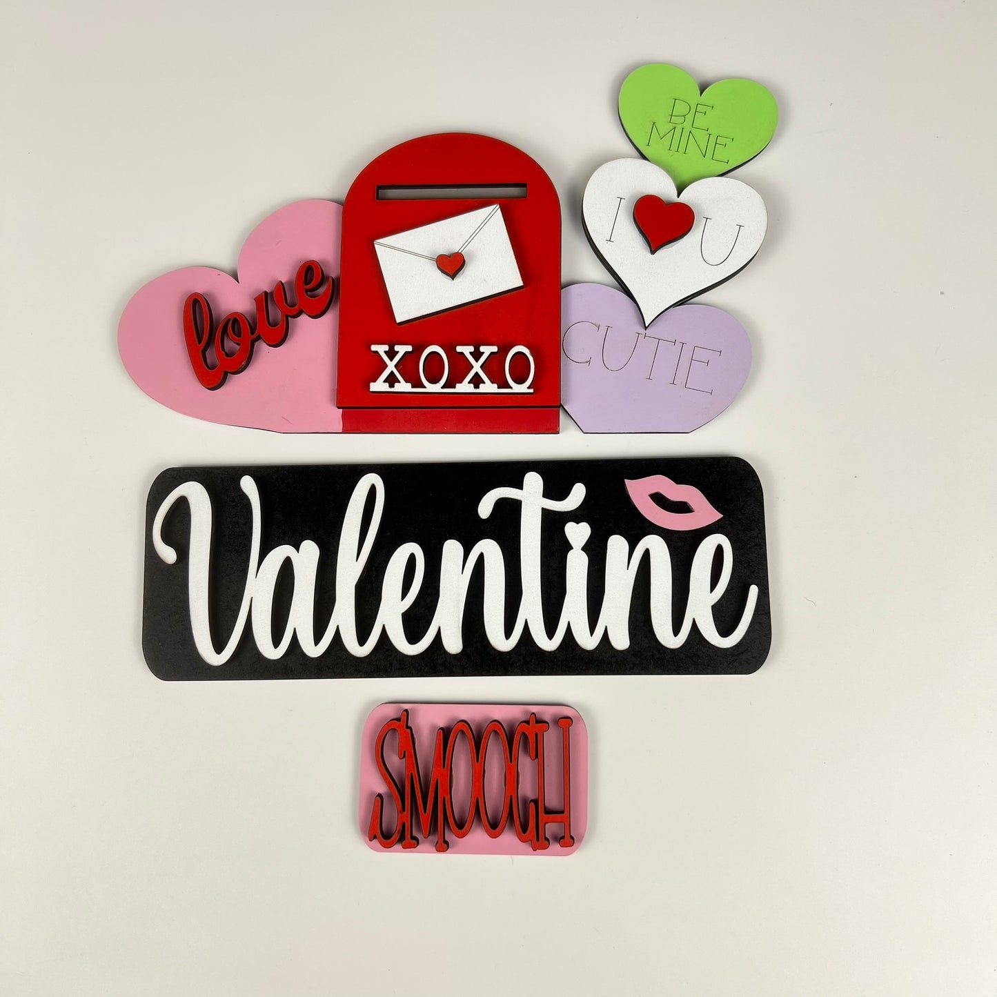 Celebrate Valentine's Day with the Valentine Interchangeable Insert - Painted from Janet's Craft Corner. This charming decorative arrangement includes a red mailbox embellished with hearts and sweet messages such as "love" and "XOXO," alongside a black and white sign featuring the word "Valentine" with a pink kiss mark. Perfect for adding rustic charm to your home, this piece offers versatile decor options for seasonal joy.