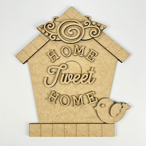 Introducing the Home Tweet Home Birdhouse Door Hanger by Janet's Craft Corner. This beautifully crafted plaque is shaped like a birdhouse and adorned with intricate designs. It features the charming words "Home Tweet Home" and includes a small bird cutout in the bottom right corner, making it an ideal addition to enhance your home décor with a delightful touch of charm.