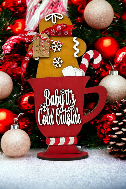 Create a cozy holiday decor with Janet's Craft Corner's Gingerbread Hot Cocoa Mug Shelf Sitter. This DIY kit includes a red "Baby It's Cold Outside" mug, gingerbread figure, candy canes, and is accented with red and gold ornaments and snowy touches.