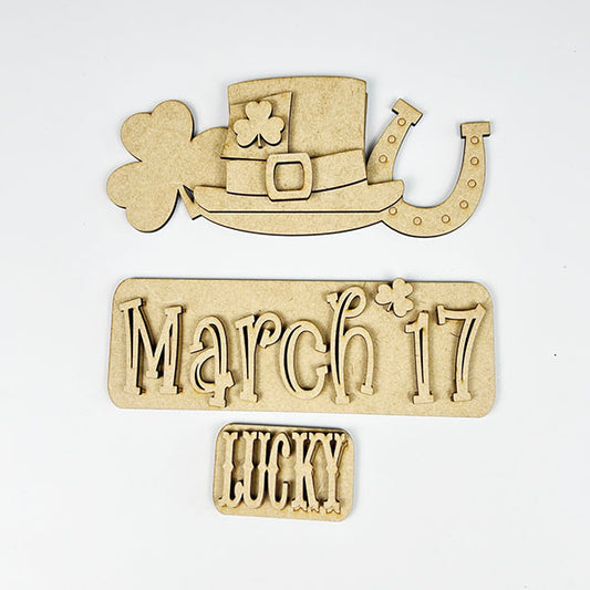 Celebrate St. Patrick's Day with Janet's Craft Corner's March 17 Interchangeable Insert, a DIY home decor kit featuring laser-cut wooden pieces such as a leprechaun hat, shamrock, and horseshoe. This hand-painted craft set includes components with the text "March 17" and "Lucky," all set against a plain background for festive charm.