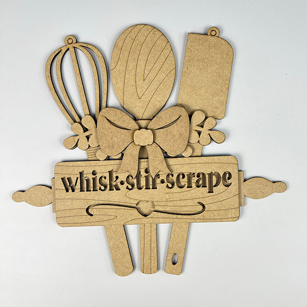 Janet's Craft Corner offers the "Whisk Stir Scrape Utensils Sign," a wooden kitchen-themed DIY décor kit featuring a whisk, spoon, spatula, and cutting board tied with a bow. A rolling pin below reads "whisk · stir · scrape" amidst decorative elements—ideal for home or as a door hanger.