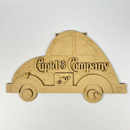 The Cupid Volkswagen Door/Wall Hanger by Janet's Craft Corner features a vintage car wooden cutout with "Cupid & Company," small hearts, and a central heart with an arrow. Ideal for DIY projects, it stands elegantly against a white background.