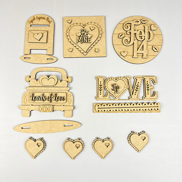 The Loads of Love Decor Set by Janet's Craft Corner is a delightful DIY kit featuring six Valentine-themed wooden pieces, including a mailbox, hearts, "Loads of Love" truck, and signs with "Be Mine," "Love," and "Feb 14." Perfect for enhancing home décor on a neutral background.