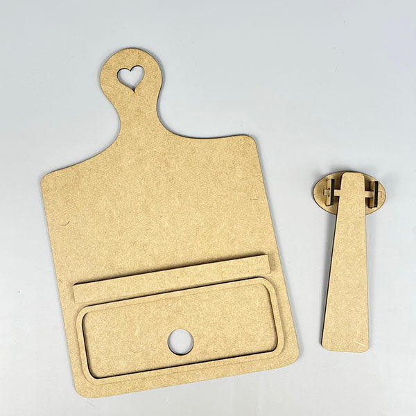 Two brown MDF pieces are displayed on a white background, crafted as part of the "Interchangeable Breadboard with Interchangeable Insert" DIY home decor kit by Janet's Craft Corner. One piece resembles a cutting board with a heart-shaped hole at the top and a rectangular slot, while the other is an interchangeable stand component designed to fit into the board.