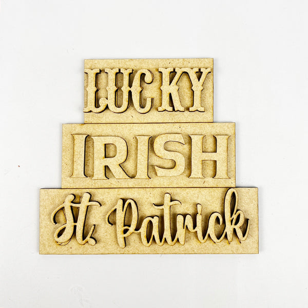 The "St Patricks Decor Set" by Janet's Craft Corner is a DIY kit featuring tiered tray wooden signs with the words "LUCKY," "IRISH," and "St. Patrick" in varied fonts on a light background, perfect for festive home decor.