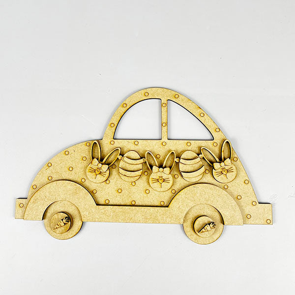 This Easter, Janet's Craft Corner offers the Easter Volkswagen Shelf Sitter as delightful home décor: a wooden car cutout with four windows of bunny shapes and eggs. The round wheels are adorned with carrot designs for festive creativity—all set on a crisp white background.