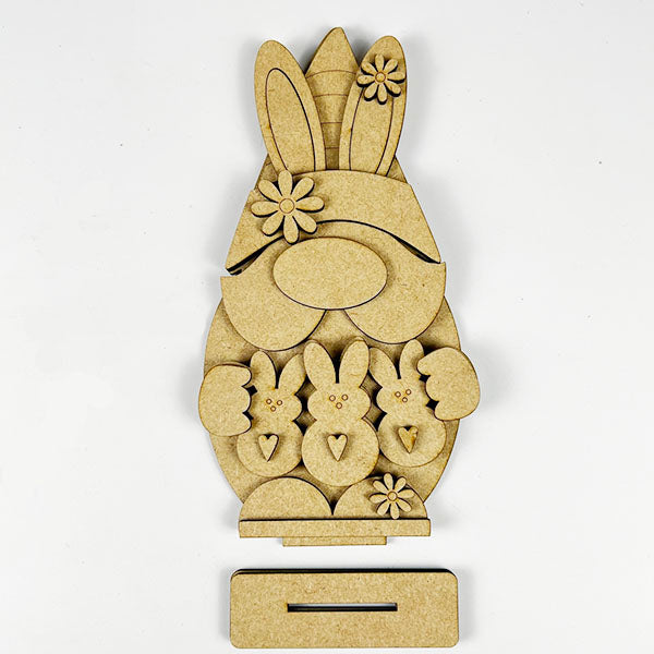 The Easter Peep Gnome Shelf Sitter DIY kit from Janet's Craft Corner features a wooden bunny holding three smaller bunnies, with floral ears and a rectangular base, perfect as a charming and simple centerpiece for Easter decorations.