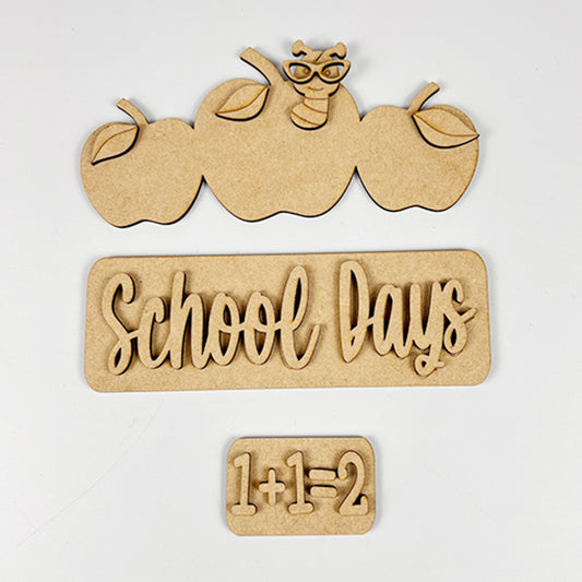 Add a touch of whimsy to your farmhouse decor with Janet's Craft Corner's School Days Interchangeable Insert. This DIY home decor kit features wooden cutouts of three apples with a worm wearing glasses, the phrase "School Days," and the equation "1+1=2," all set against a plain background.