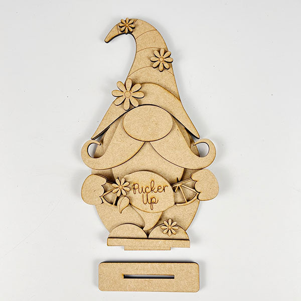 Janet's Craft Corner offers a charming Lemonade Gnome Shelf Sitter DIY home decor kit. This wooden gnome figure with a floral hat and beard holding a "pucker up" sign adds whimsical farmhouse flair, featuring an easy DIY setup thanks to the slot at the bottom.