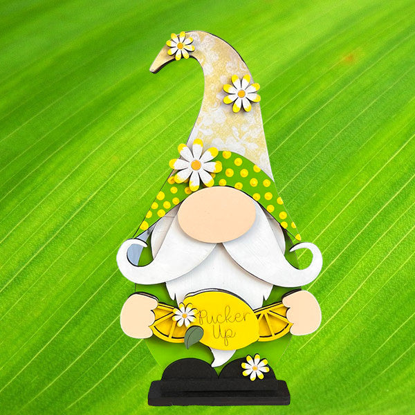 Janet's Craft Corner presents the Lemonade Gnome Shelf Sitter, a DIY home decor kit featuring a charming gnome with a tall yellow hat adorned with daisies on a vibrant green background. Holding a "Pucker Up" lemon slice, it adds whimsy to farmhouse decor.