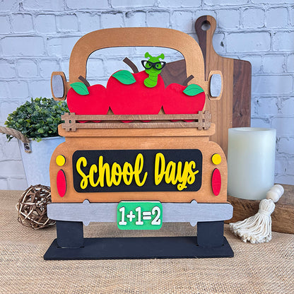 Introducing the DIY home decor kit by Janet's Craft Corner: Antique Truck Base with Interchangeable Insert! This charming decorative sign features an antique truck adorned with apples and a worm in glasses in the bed. The tailgate playfully reads "School Days," and the license plate is marked with "1+1=2." Display it on a table alongside a plant and candle for a perfect hand-painted craft project.