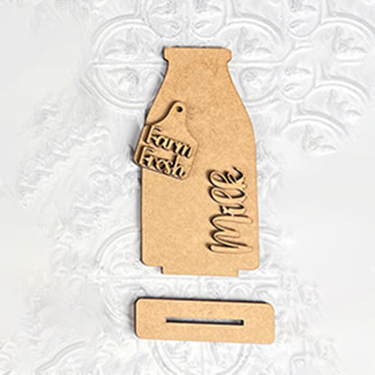 Janet's Craft Corner presents the Farm Standing Shelf Sitter—a wooden cutout of a milk bottle featuring "Farm Fresh" on a tag and "milk" inscribed on the bottle. This decorative piece is perfect for your farmhouse decor, elegantly displayed on a textured white surface, complete with a separate rectangular base to add a rustic touch.