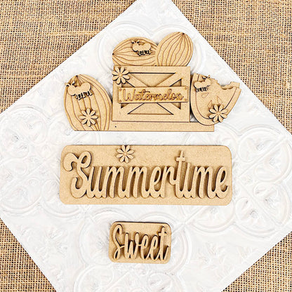 Wooden accents on a textured backdrop: featuring a "Summertime" sign with a sun, a "Sweet" sign, and a crate marked "Watermelon," complete with decorated slices and flowers from the Summertime Watermelon Interchangeable Insert by Janet's Craft Corner—a perfect blend of farmhouse style for your hand-painted DIY home decor kit.