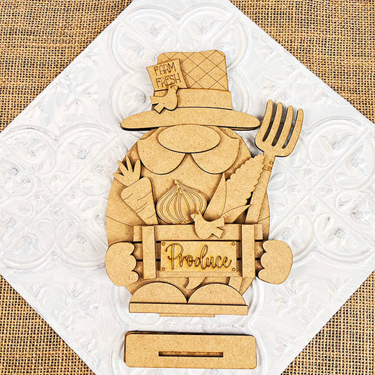 Add rustic charm to your farmhouse décor with Janet's Craft Corner's Farmer Gnome Shelf Sitter. This DIY home decor craft kit features a gnome farmer with a "Farm Fresh" hat, pitchfork, and "Produce" box filled with carrots and onions against a white tile-textured burlap backdrop.