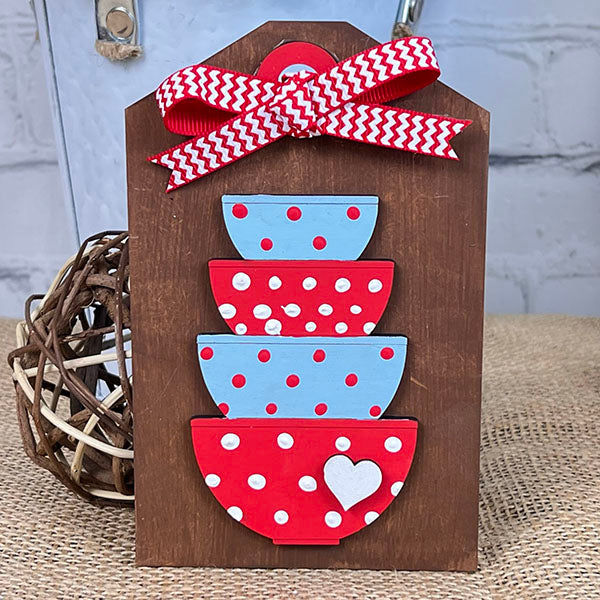 The Baking - Tiered Tray Kit from Janet's Craft Corner features a decorative wooden plaque displaying three polka dot bowls in blue and red, topped with a red and white chevron ribbon. A small white heart embellishes the bottom bowl, while a wicker ball enhances the rustic farmhouse decor atmosphere in the background.