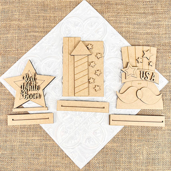 Janet's Craft Corner offers wooden patriotic shelf sitters with burlap details: a star with "Red White Boom," a starry firework, and a hat with "USA" and mustache, each on an embossed white square base. Perfect for farmhouse decor or DIY kits.