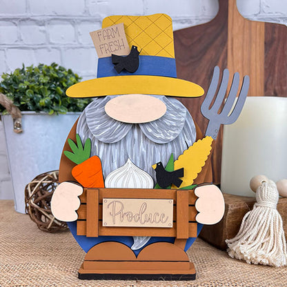 Introducing the Farmer Gnome by Janet's Craft Corner, a delightful decorative figure featuring a gray beard and yellow hat. This charming gnome holds a carrot, corn, and a "Produce" sign, while a small black bird perches on his hat as he grips a pitchfork. He seamlessly complements your rustic kitchen décor with his farmhouse charm.