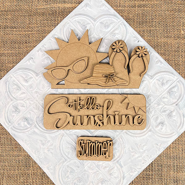 The Hello Sunshine Interchangeable Insert by Janet's Craft Corner is a delightful wooden plaque kit that features a sun with sunglasses, a hat, and flip-flops decorated with flowers. The phrases "Hello Sunshine" and "Summer" stand out against its textured white background, providing a cheerful addition to your home decor.