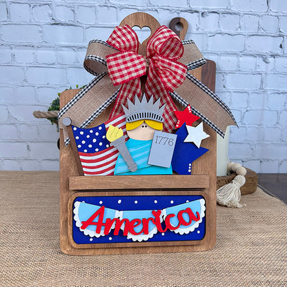 The "America Interchangeable Insert" from Janet's Craft Corner adds Americana charm to your home decor with its festive wooden plaque design. Featuring a red, white, and blue theme, it includes the word "America," a small Statue of Liberty figure, a red gingham bow, and star accents. Additionally, it comes with a miniature Declaration of Independence marked with "1776." Ideal for interchangeable inserts on any brick wall.