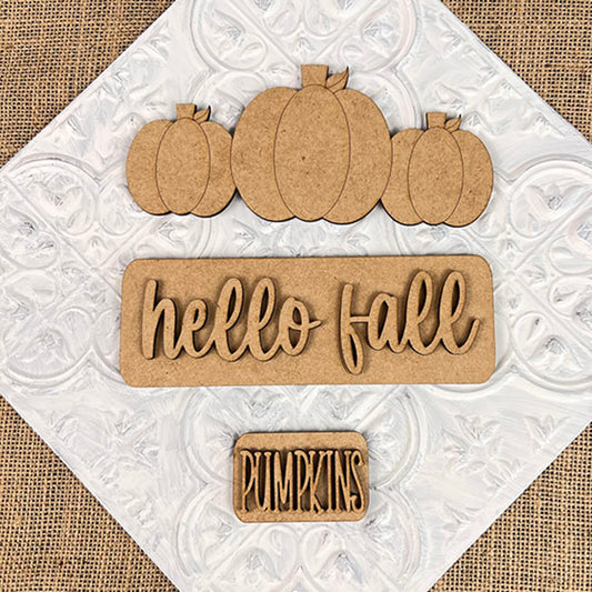 This delightful seasonal decor, part of the "Hello Fall Interchangeable Insert" DIY home decor kit by Janet's Craft Corner, features wooden cutouts of three pumpkins, a "Hello Fall" sign, and a small "pumpkins" sign on a white background with a subtle floral pattern—ideal for your crafting projects.