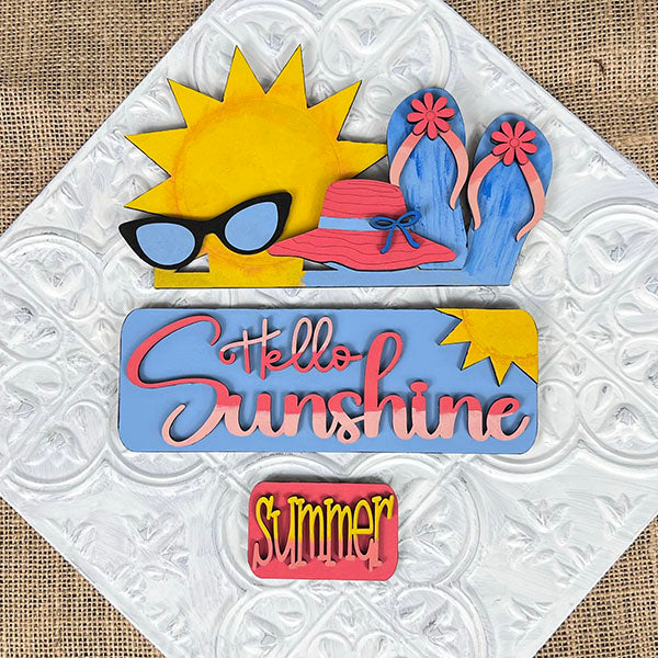 The Hello Sunshine Interchangeable Insert by Janet's Craft Corner is a decorative DIY home decor kit that showcases summer-themed artwork, including a sun, sunglasses, flip-flops, and a hat. It features the text "Hello Sunshine" and "Summer" set against a textured background, making it an ideal choice for crafting enthusiasts to create hand-painted projects for their homes.