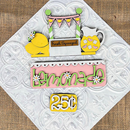 The "Lemonade Interchangeable Insert," part of Janet's Craft Corner DIY home decor kit, features vibrant cutouts of lemons, a pitcher, and a banner. Ideal for enhancing your living space, it sits on a textured white background that mimics embossed tin.