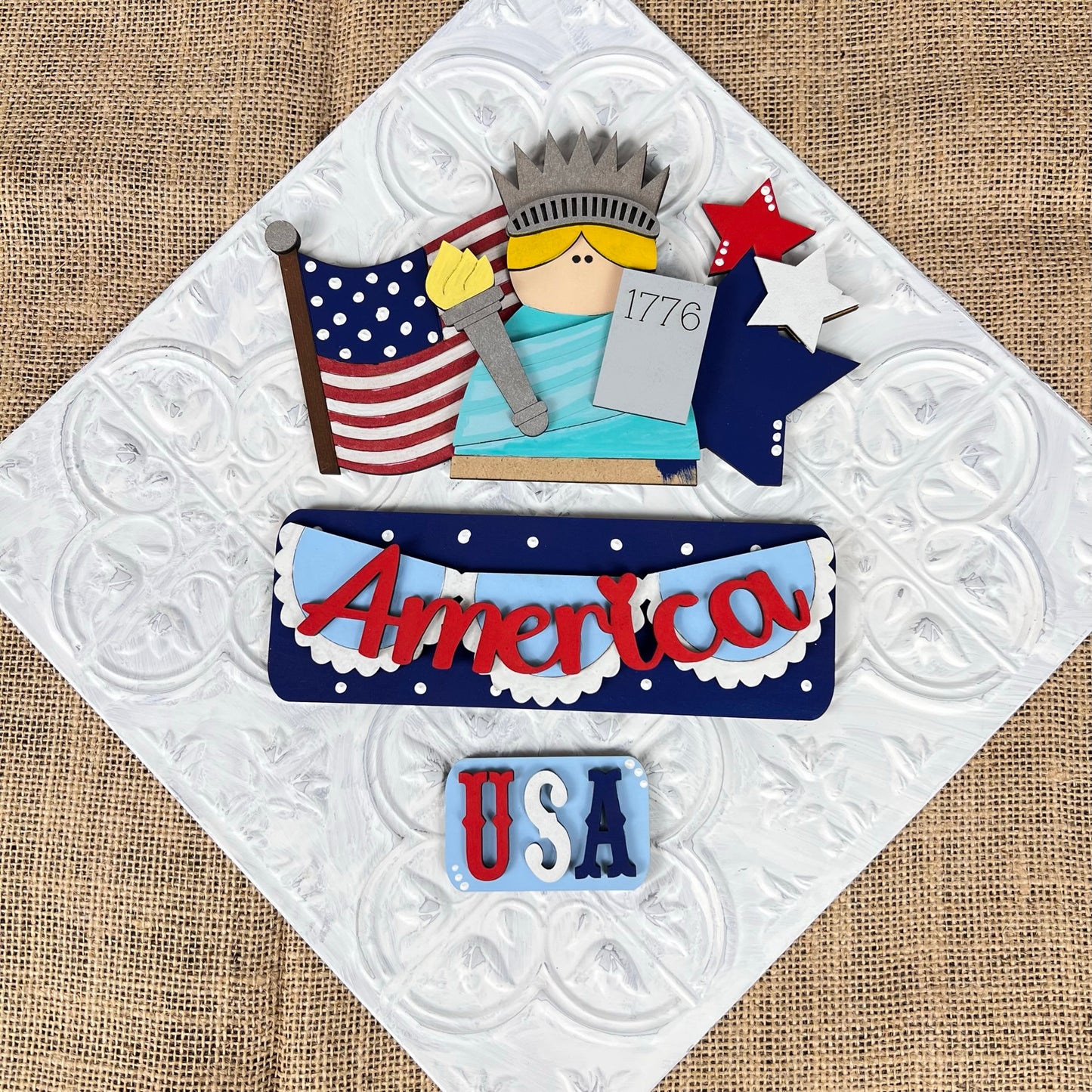 The America Interchangeable Insert from Janet's Craft Corner is a DIY home decor kit featuring a wooden cutout of the Statue of Liberty with "1776" on her tablet, accompanied by a flag and star. The textured background includes "America" and "USA" in red, white, and blue, making it an ideal choice for DIY Craft Kit enthusiasts who enjoy interchangeable inserts.