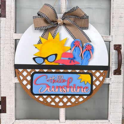 The "Hello Sunshine" Interchangeable Insert from Janet's Craft Corner offers a delightful DIY home decor kit, perfect for hanging on your door. This hand-painted round sign showcases a playful sun wearing sunglasses, accompanied by a sunhat and flip-flops. The vibrant lettering spells out "Hello Sunshine," while the charming burlap and gingham bow completes the look of this interchangeable piece.