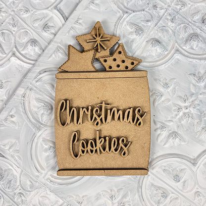 The Vintage Santa Cookies Tiered Tray Set by Janet's Craft Corner features a charming vintage-style wooden ornament of a cookie jar labeled "Christmas Cookies," adorned with three star-shaped treats. It's perfect for enhancing your holiday display and pairs beautifully with any tiered tray set against a decorative textured background.