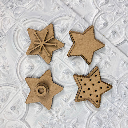 Displayed on a textured white background are four star-shaped wooden ornaments from Janet's Craft Corner, featuring various cut-out designs including a starburst, a plain star, a circle, and small holes. They're perfect for the Vintage Santa Cookies Tiered Tray Set.