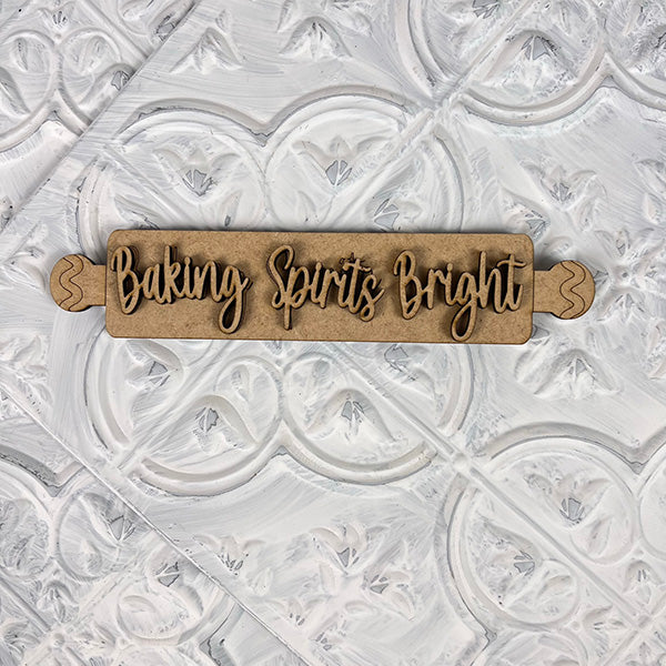 A rolling pin engraved with "Baking Spirits Bright" by Janet's Craft Corner lies on a textured white background, adding a nostalgic charm to your Vintage Santa Cookies from the Tiered Tray Set.