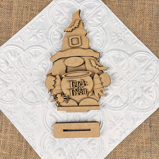 Janet's Craft Corner offers the Witch Gnome Shelf Sitter, a DIY seasonal home decor craft kit. This wooden Halloween decoration features a witch gnome in a pointed hat with a "Trick or Treat" cauldron on an embossed white burlap background and includes an easy assembly slot.