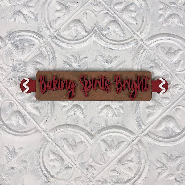 Introducing the Vintage Santa Cookies Tiered Tray Set by Janet's Craft Corner: a charming wooden rolling pin featuring red handles and the festive phrase "Baking Spirits Bright" in elegant red cursive script. This delightful piece is perfect for your DIY Kit and is beautifully showcased against a textured white background with an ornamental pattern.