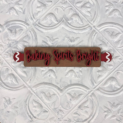 Introducing the Vintage Santa Cookies Tiered Tray Set by Janet's Craft Corner: a charming wooden rolling pin featuring red handles and the festive phrase "Baking Spirits Bright" in elegant red cursive script. This delightful piece is perfect for your DIY Kit and is beautifully showcased against a textured white background with an ornamental pattern.