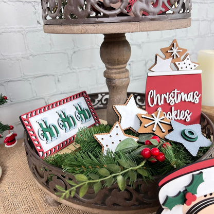 Janet's Craft Corner presents the Vintage Santa Cookies Tiered Tray Set, featuring Christmas-themed decorations such as a "ho ho ho" sign and vintage Santa cookies in star and tree shapes. The set is accented with pine branches and red berries, making it an ideal choice for those who enjoy festive seasonal DIY kits.