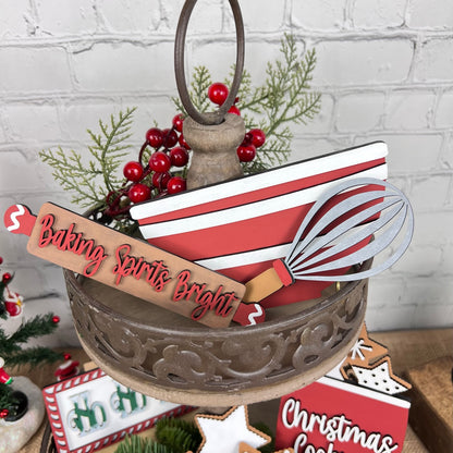 The Vintage Santa Cookies Tiered Tray Set by Janet's Craft Corner is a charming display adorned with Christmas-themed items, showcasing a red and white striped sign, a whisk cutout, and a "Baking Spirits Bright" sign. This delightful arrangement includes artificial red berries, greenery, vintage Santa cookies, and features snowflake and gingerbread decorations.