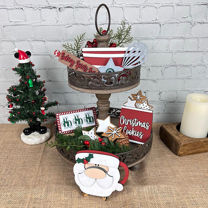 The Vintage Santa Cookies Tiered Tray Set from Janet's Craft Corner is beautifully adorned with holiday-themed items, featuring a Vintage Santa Cookies sign, gingerbread ornaments, and a small potted tree. A lit candle and another small Christmas tree complete the warm and festive display.