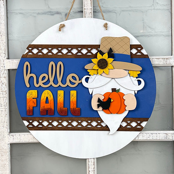 The Gnome Hello Fall Door Hanger from Janet's Craft Corner lets you create an enchanting round wooden sign. It features a gnome in a tan hat holding a pumpkin, with the phrase "Gnome Hello Fall" in decorative font. The blue background and brown lattice border add warmth to your home décor, and the gnome’s hat is adorned with a sunflower.