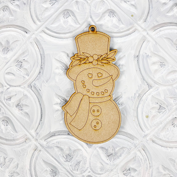 Janet's Craft Corner presents the Color Your Own Ornament DIY Decoration Kits, featuring a wooden snowman adorned with a hat, scarf, and holly embellishment, ideal for your Home Décor Craft projects against a decorative white backdrop.