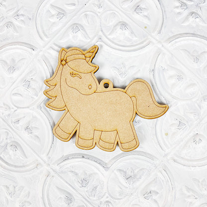 A cutout of a unicorn, crafted from wood with intricate details, is featured on an embossed white background. This Color Your Own Ornament kit from Janet's Craft Corner includes decorative elements like a flower near the ear and a built-in hole for hanging, making it ideal for home décor craft enthusiasts.