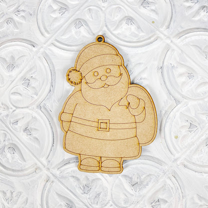 Introducing the Color Your Own Ornament from Janet's Craft Corner, a stylish wooden Santa Claus ornament that is perfect for any DIY Decoration Kit. Featuring a classic hat, belt, and sack, it boasts a smooth finish and complements a textured white background beautifully, adding charm to your home décor craft collection.