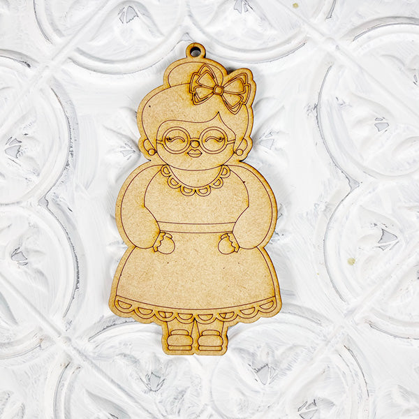 The Color Your Own Ornament DIY Decoration Kit by Janet's Craft Corner showcases a charming wooden cartoon grandmother, complete with glasses, a bow in her hair, and a dress. The detailed cut-out designs add to its appeal against a textured white background. This kit offers the perfect opportunity for a home décor craft project where you can create your unique ornament masterpiece.