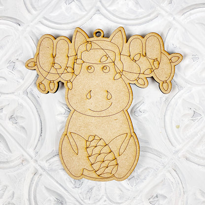 Introducing Janet's Craft Corner's Color Your Own Ornament DIY Decoration Kit: a wooden moose ornament beautifully enhanced with carved details and a small pinecone between its legs, set against a textured white background. Ideal for adding charm to your home décor craft collection.