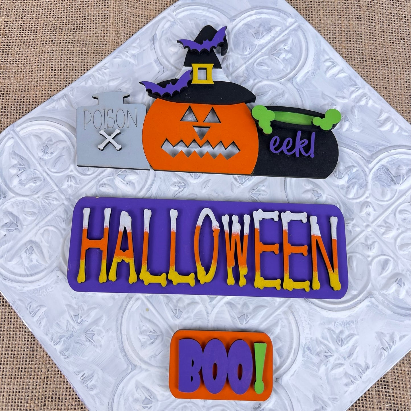 Transform your space into a spooky scene with Janet's Craft Corner's Halloween Pumpkin Interchangeable Insert DIY home decor kit. It includes a pumpkin, witch's hat, and cauldron labeled "eek!" Enhance the frightful atmosphere with a sign that screams "POISON." Personalize the vibrant "HALLOWEEN" display and switch out interchangeable inserts to keep your wooden backdrop fresh and exciting all season long.