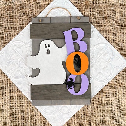 The Boo Fence Door Hanger from Janet's Craft Corner is a versatile DIY kit. It showcases a wooden white ghost silhouette next to vibrant "B," "O," and "O" letters in purple and orange. Ideal for your door, it enhances your home décor with its festive touch and burlap-textured background.