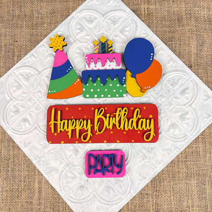 Janet's Craft Corner presents the Birthday Interchangeable Insert DIY home decor kit, which includes vibrant decorations such as a cake with candles, a party hat, balloons, and two signs that read "Happy Birthday" and "Party," all set against a textured white background. Ideal for DIY craft enthusiasts and interchangeable home decor projects.