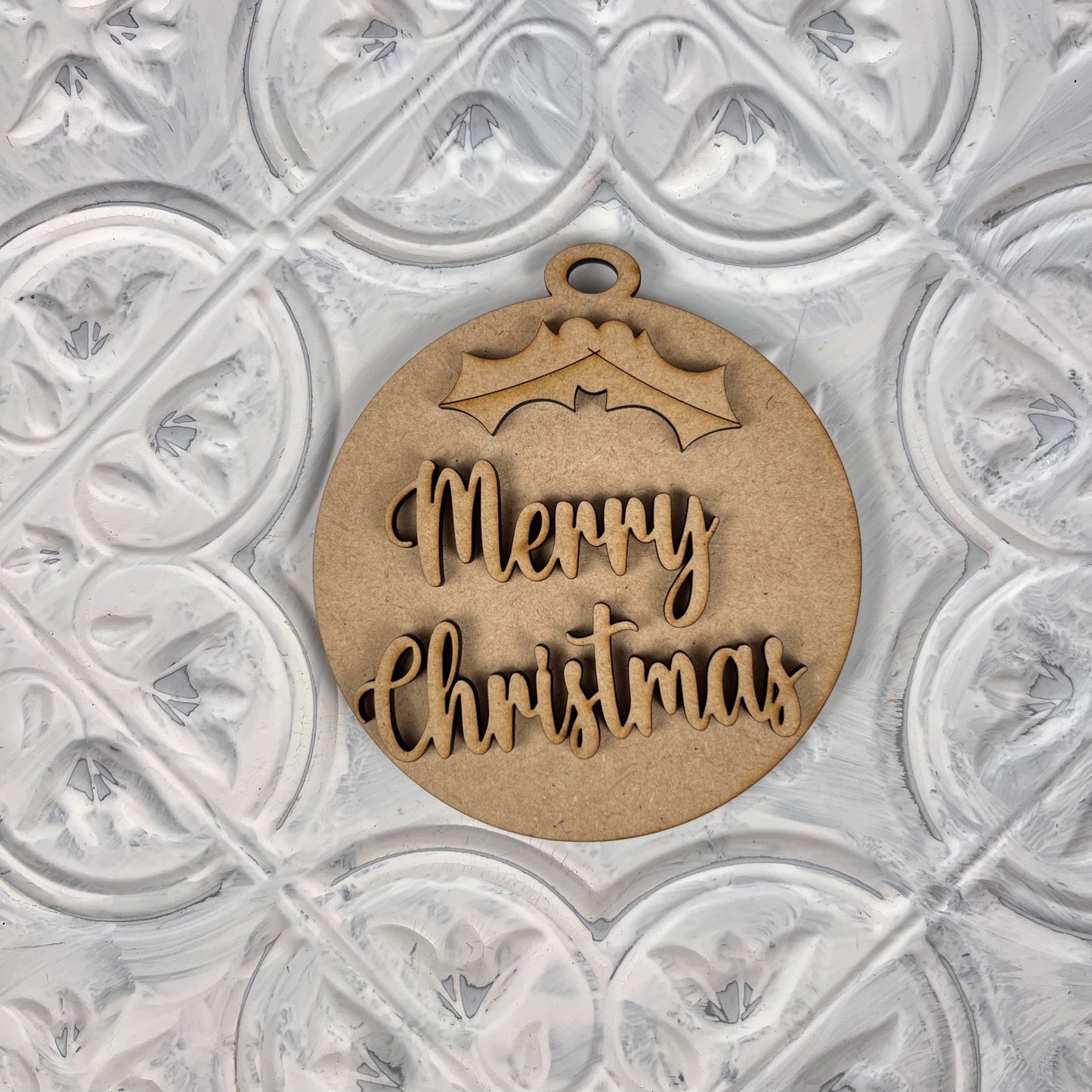 A "Round Christmas Ornament" from Janet's Craft Corner's DIY Decoration Kits complements your home décor when placed elegantly on a decorative white textured surface. Featuring a charming holly design at the top, this ornament adds a festive touch to any setting with its "Merry Christmas" text.